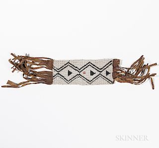 Plains Beaded Hide Armband, c. 1880s, black and red beaded design on white ground, with long hide fringe at either end, lg. 18 1/2, wd.
