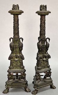 Pair of bronze candlesticks with flaming nozzle over foliate shaft flanked by three storks and ram's head mask supports on triangula...