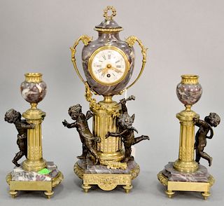 Three piece French clock set having bronze putti, rouge marble, and porcelain dial. clock ht. 12 1/2 in., candlestick ht. 8 1/4 in.