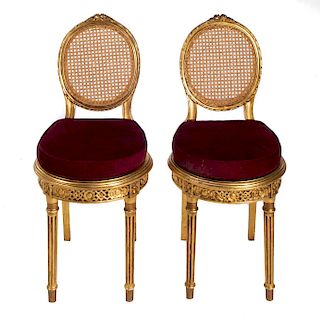 Par de sillas. En talla de madera dorada. Con respaldo de bejuco, fustes acanalados, soportes tipo carrete y asiento de tela color vino
