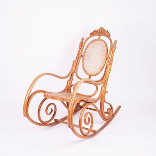 Mecedora. Siglo XX.  Estilo austriaco. En madera tallada y barnizado natural de acabado brillante. Con respaldo y asiento de bejuco.