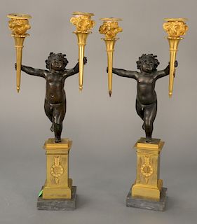 Pair of bronze figural candlesticks, 
having winged putti figure holding gilt bronze torch form candle holders standing on square pl...