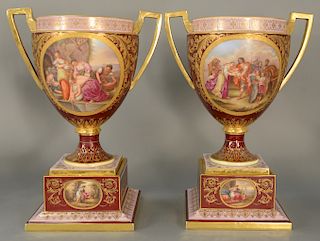 Pair of Royal Vienna porcelain urns, 
each having gilt handles with hand painted panels, set on square bases with painted panels, ar...