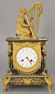 Bronze and gilt bronze French clock mounted with seated woman playing harp over draped clock face supported by columns with woman's ...