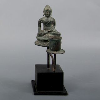 Candelero. Origen oriental. Siglo XX. Elaborado en bronce. Con base de madera tallada. Decoración del Príncipe Siddharta Gautama.