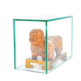 Almohadilla*. China, siglo XVIII/XIX. Talla en madera. Con base de bronce y capelo de vidrio. Diseño a manera de personaje reclinado.
