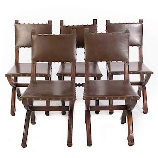 Lote de 5 sillas. SXX. En talla de madera. Con tapicería de piel color marrón. Respaldo cerrado, fustes en "X" y soportes tipo bollo.