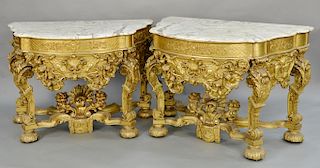 Pair of gilt Louis XIV style console tables with shaped marble tops, over conforming frieze on carved and scrolled legs, set on modi...