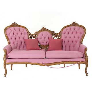 Love seat. Origen europeo. Siglo XX. Estilo Luis XV. En talla de madera. Con tapicería de tela color rosado. Repaldo capitonado.