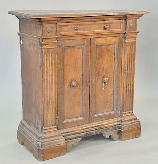 Continental walnut cabinet having rectangular top over one drawer over two doors flanked by fluted pilasters, set on step molded bas...