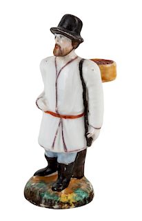 A RUSSIAN PORCELAIN FIGURE OF A TRAVELER WITH A BASKET OF BERRIES, PRIVATE PORCELAIN FACTORY, MID-19TH CENTURY