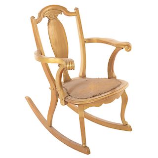 Mecedora. Siglo XX En talla de madera dorada. Con respaldo semiabierto, asiento con tapicería color ocre, fustes y soportes semicurvos.