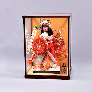 Muñeca. Origen oriental. SXX. Estilo Geisha. Elaborada en pasta. En caja de vidrio. Con ojos de vidrio, cabello sintético, vestida.