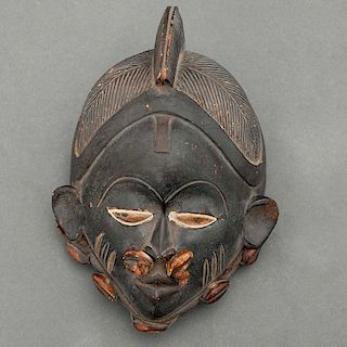Máscara femenina. Nigeria, Siglo XX. Grupo étnico Igbo. Elaborada en terracota, conchas de cauri y fibras naturales.
