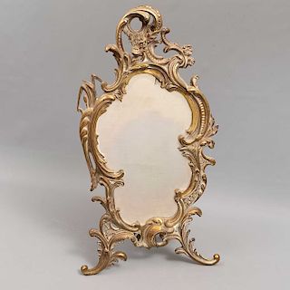 Espejo para tocador. SXX. Estilo Art Nouveau. Elaborado en latón. Con espejo de luna irregular biselada y soportes a manera de roleos.