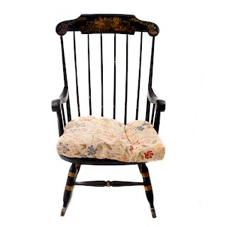 Mecedora. Elaborada en madera tallada. Respaldo con barandillas, asiento liso con almohadón en textil floral y chambrana de caja.
