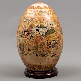 Huevo. Origen oriental. Siglo XX. Elaborado en cerámica. Con base de madera tallada. Dimensiones: 22 x 15 cm. Ø