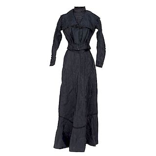BLOUSE AND SKIRT SET. CIRCA 1900. Black blouse with standing collar. Details in lace and plaited cords. Matching pleated skirt.  