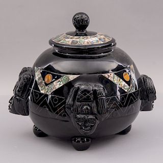Urna. México, siglo XX. Elaborada en mármol negro pulido con aplicaciones de concha de abulón. Decorada con mascarones.