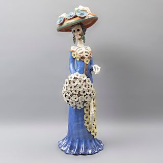 Catrina. México. Siglo XX. Elaborada en barro policromado. Vestida con vestido azul, sombrero, aretes y ramo de flores. 71 x 22 x 26 cm
