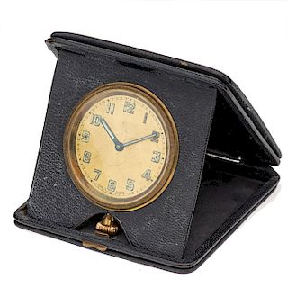 Reloj de viaje sin marca. Movimiento manual. Caja circular en acero dorado. Carátula color cobre. Base en vinil color negro.