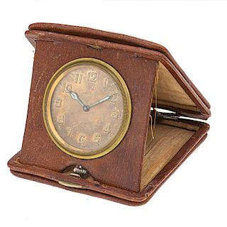 Reloj de viaje sin marca. Movimiento manual. Caja circular en acero dorado. Carátula color cobre. Base en vinil color café.