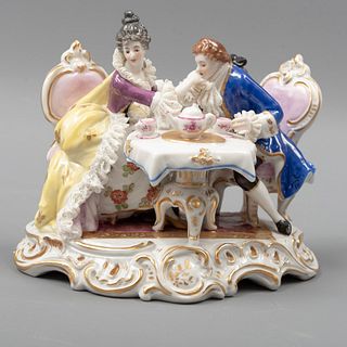 Pareja cortesana. Siglo XX. En porcelana. Decorados con mesa, juego de té, sillas, elementos orgánicos y esmalte dorado. 10 x 13 x 9 cm