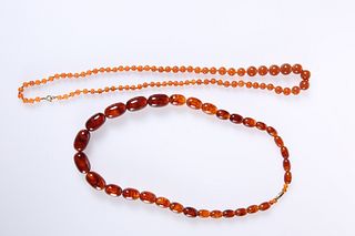 TWO STRINGS OF AMBER COLOURED BEAD NECKLACES, the first of graduating oval 