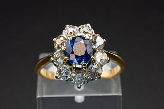 A SAPPHIRE AND DIAMOND CLUSTER RING, the oval cut sapphire set within a sur