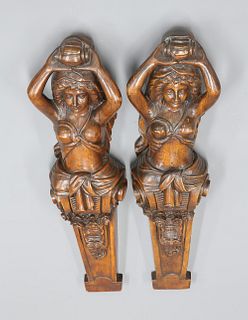 A PAIR OF CARYATID CARVINGS, each scantily clad female half-length with arm