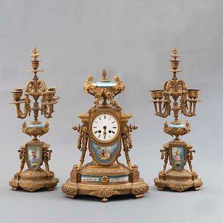Guarnición. Francia. Siglo XX. Elaborada en bronce y cerámica. Consta de: Reloj de mesa y par de candelabros. 53 x 18 x 12 cm. Pzs: 3.