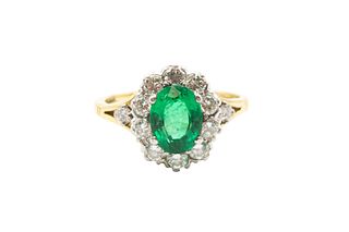 AN EMERALD AND DIAMOND CLUSTER RING
 Centrally-set with an oval-cut emerald