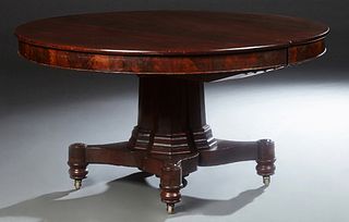 American Empire Carved Mahogany Oval Dining Table, 19th c., with a wide skirt, on a dodecahedron pedestal to a quadruped base on tur...