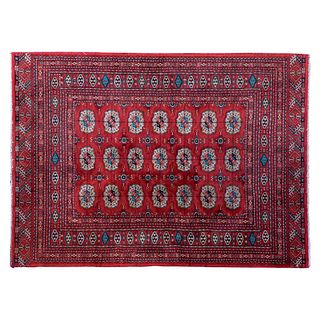 Tapete. Pakistán. Siglo XX. Estilo Boukhara. Elaborado en fibras de lana y algodón. Decorado con sobre fondo rojo.