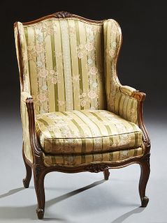 French Louis XV Style Carved Walnut Wingback Bergere, early 20th c., the arched floral carved crest rail over an upholstered back, wings and arms, to 