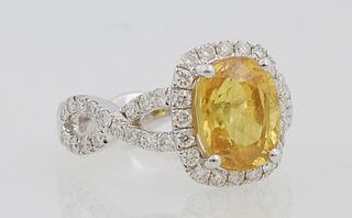 Lady's Platinum Dinner Ring, with a 4.55 ct. cushion cut yellow sapphire atop a border of small round diamonds, the split pierced infinity form should