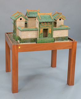 Chinese Model of a Village, green and amber glazed pottery having four houses with connected wall surround on stand in plexiglass bo...
