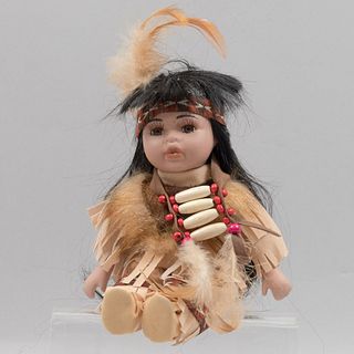 Muñeca nativa americana. Siglo XX. Elaborada en porcelana, cabello sintético, cuerpo de tela y gamuza camello.
