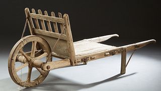French Provincial Carved Pine Primitive Wheelbarrow, 19th c., with a spiked iron rimmed wheel on one end and two handles on the othe...