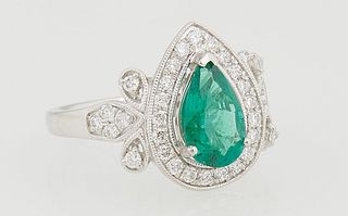 Lady's Platinum Dinner Ring, with a pear shaped 1.34 ct. emerald, atop a conforming border of small round diamonds, flanked by diamond mounted leaf lu