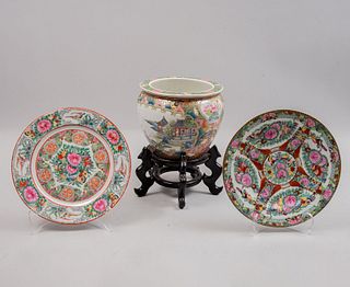 Lote de 3 piezas. China. Siglo XX. Estilo Familia Rosa. En porcelana. Consta de: maceta con base de madera y 2 platos decorativos.