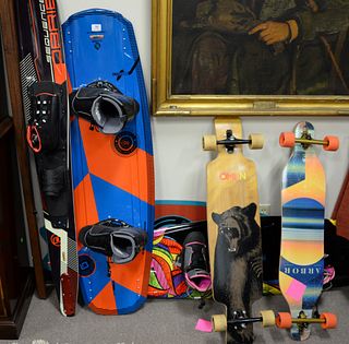 Group of sporting gear, slalom skis, two wakeboards, two long boards along with a wave board.