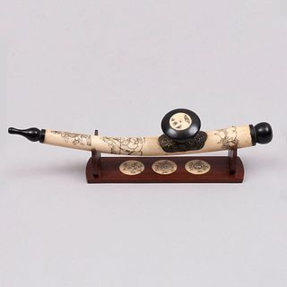 Pipa para opio. China. Siglo XX. Talla en hueso con aplicaciones de metal y de madera. Con detalle en tinta negra. Con base.