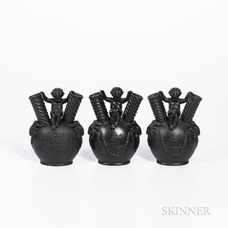 Three Wedgwood Black Basalt Figural Vases, England, 19th century, each with child seated between two twisted angular spouts atop an ovo