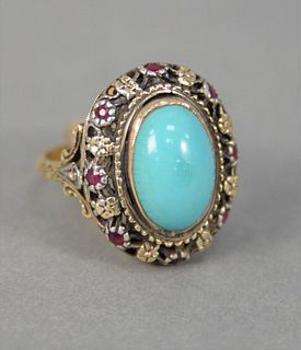 18K yellow and white gold ring stamped 18K, center is set with 1 oval turquoise surrounded by small rubies, size 6, 6.6 gr.