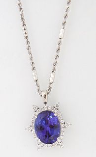 18K White Gold Pendant, with an oval 14.65 ct. tanzanite atop a border of round diamonds, the exterior mounted with six spaced diamo...