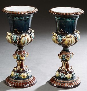 Pair of Majolica Urns, 19th c., in cobalt blue, of campana form, with relief polychromed decoration, to a socle support with relief heads, on a slopin