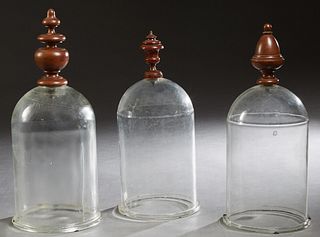 Group of Three Thick Glass Exhibition Domes, 19th c., with turned walnut finial form handles, H.- 21 1/2 in., Int. Dia.- 8 3/8 in; H.- 22 3/4 in., Int