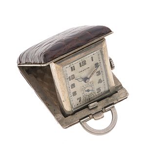 Reloj de viaje marca Orator. Movimiento manual. Caja rectangular en metal base con cubierta de piel color café. Carátula color gris.