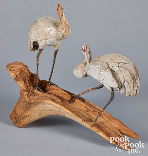 Two carved and painted egrets on a driftwood base